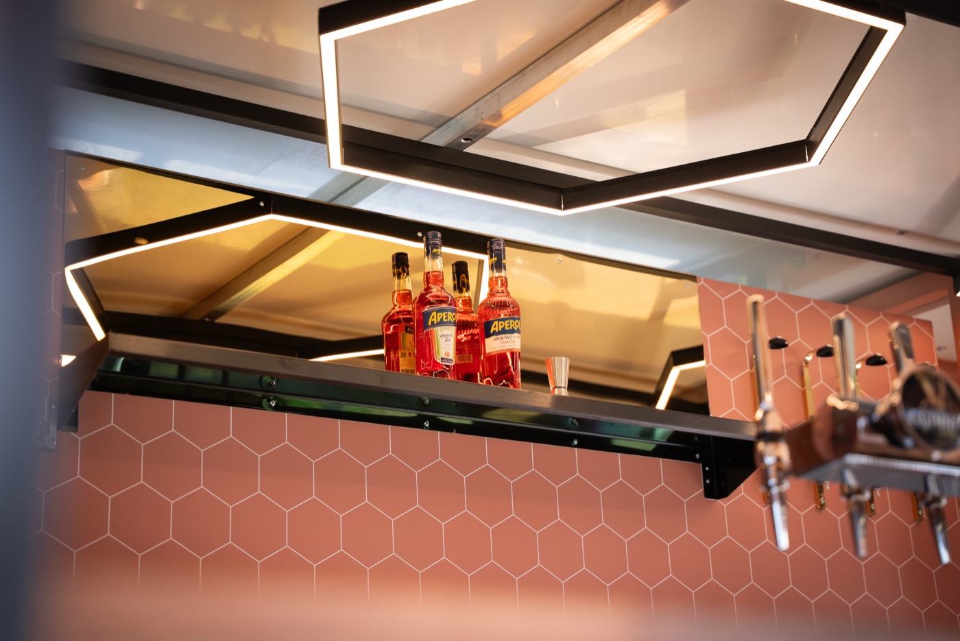 Inside The Craic Bar, taps and bottles lit up behind pink hexagon tiling